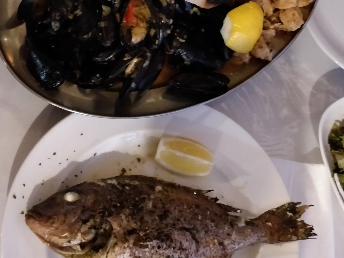 A pot of mussels beside a whole grilled fish