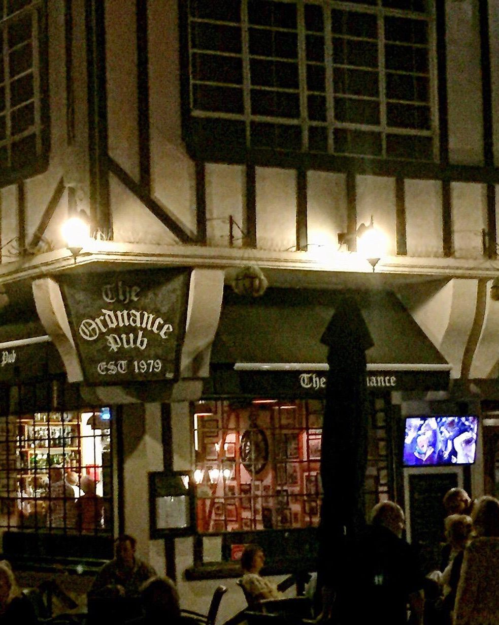 The Ordnance at night, the sign lit above a full terrace